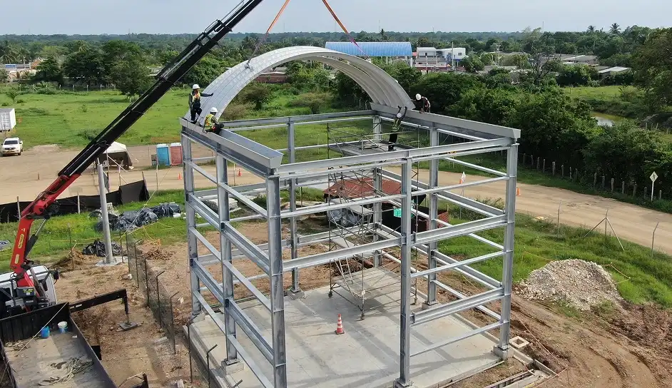 trabajadores realizando el izaje y montaje de una cubierta autoportante sobre una estructura metalica con ayuda de una grua